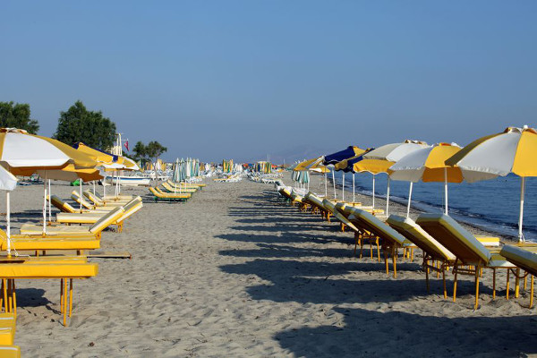 Sonnenschirme und Liegen stehen in Reihen am Strand von Tigaki